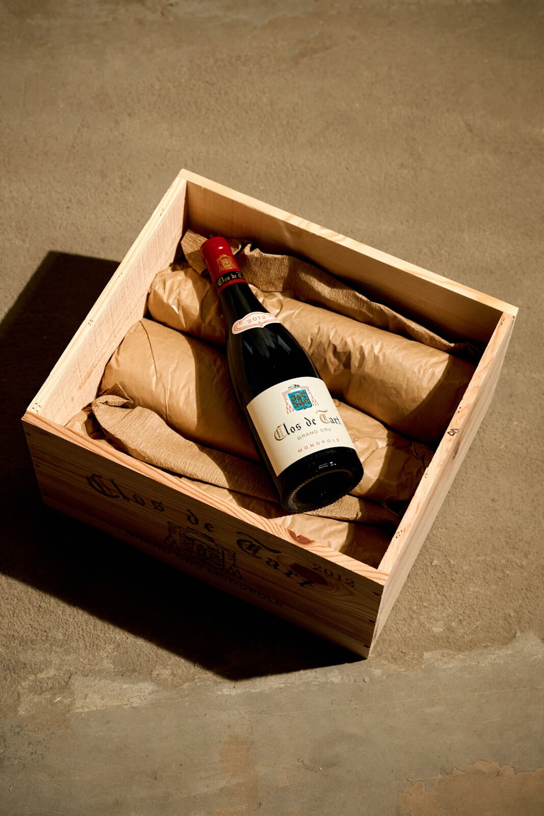 Lahev Clos de Tart Grand Cru Monopole 2012 leží v původní dřevěné bedně, vystlané balicím papírem.