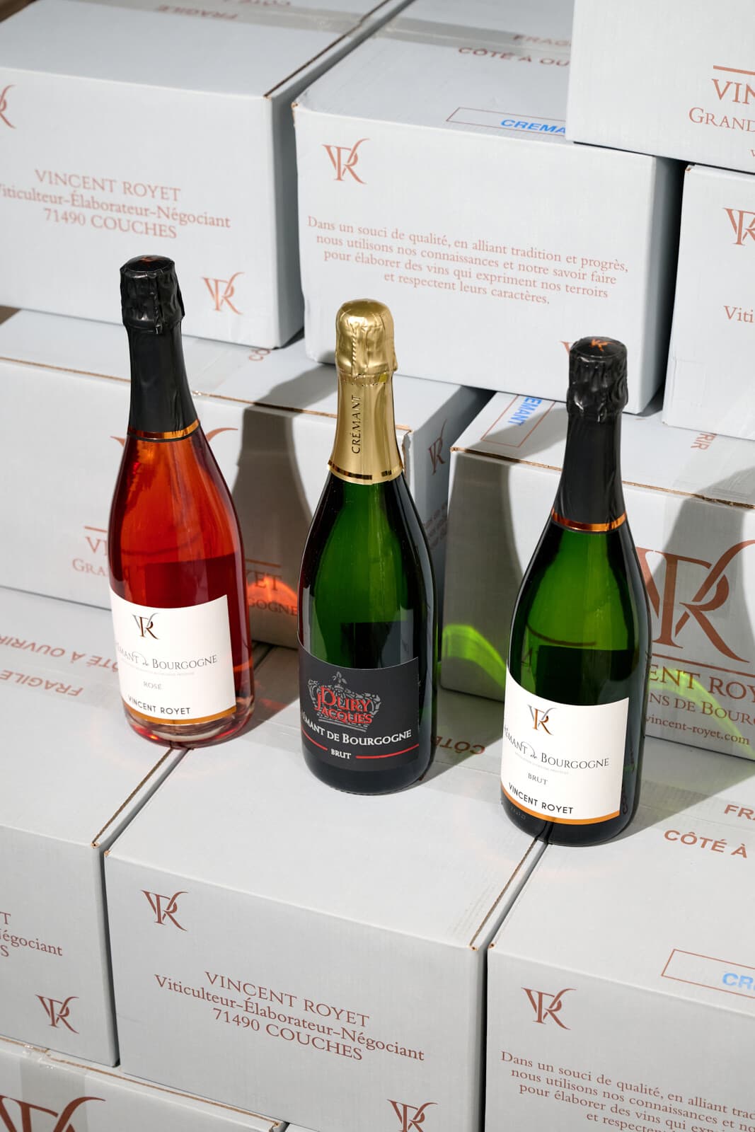 Tři lahve Crémant de Bourgogne od Vincenta Royeta (rosé, brut a blanc) na bílých kartonech domény z Couches.